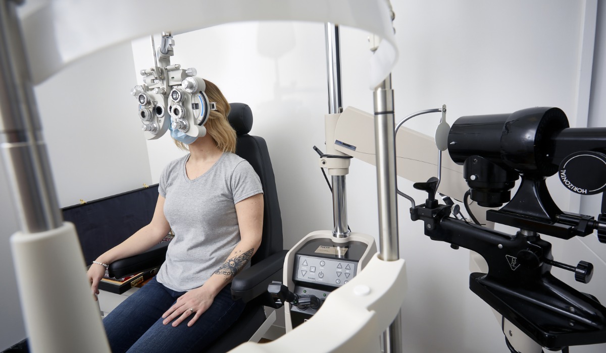 A woman undergoing an eye examination with a phoropter and other optometric equipment in a clinical setting.