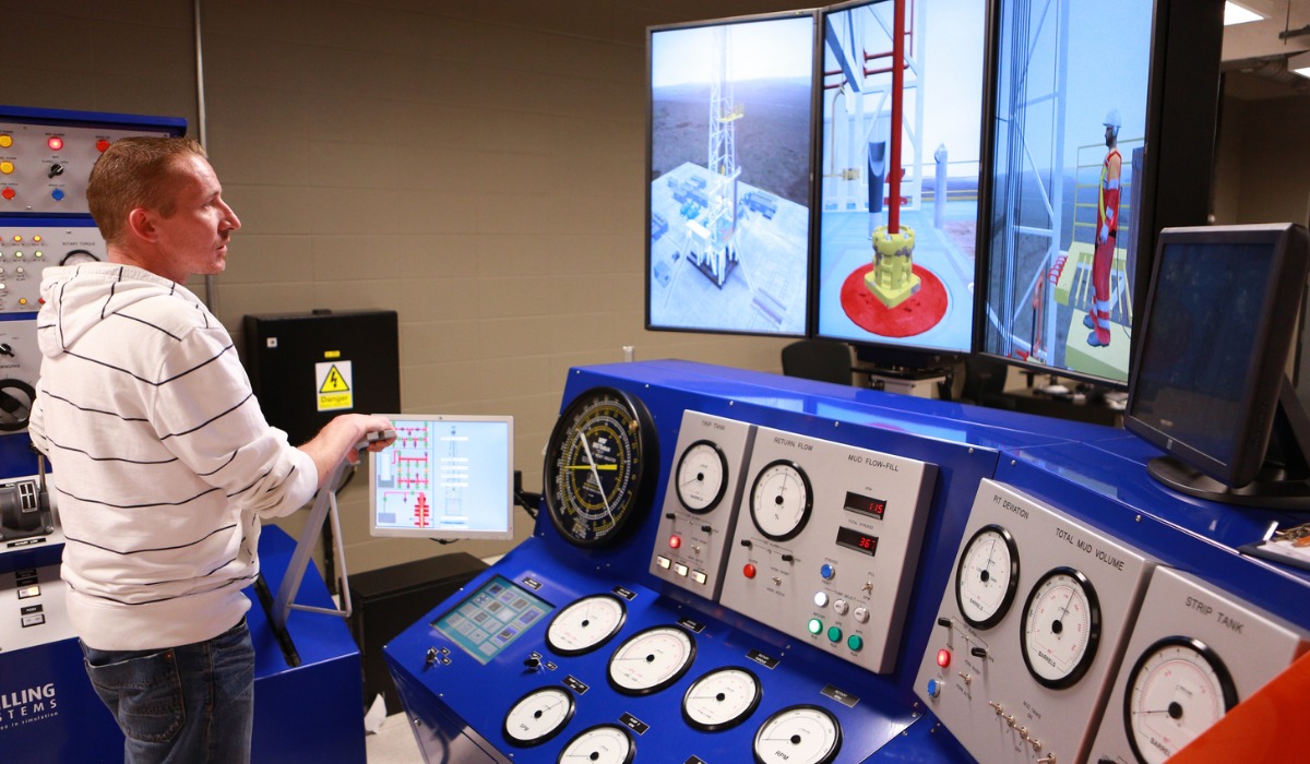 A man operates a drilling control simulator with multiple displays showcasing drilling operations and metrics.
