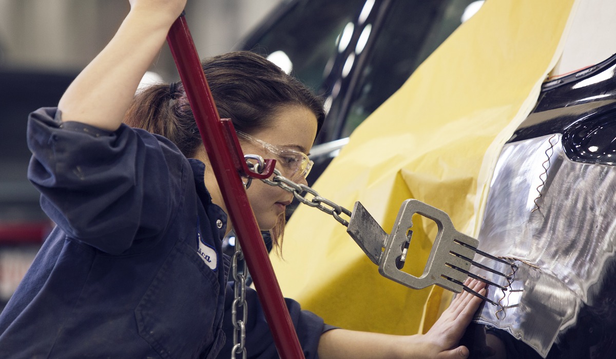 A technician using a metal puller tool to repair a vehicle's bodywork.