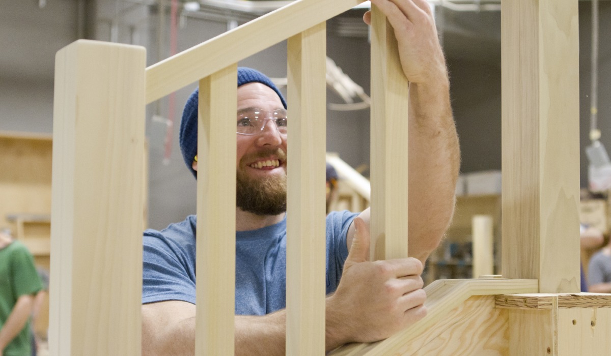 A smiling carpenter holding wooden stair components in a workshop, showcasing his woodworking skills.