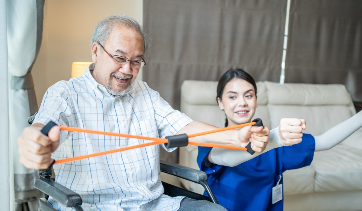 A physical therapist assists an elderly man with resistance bands during a rehabilitation session.