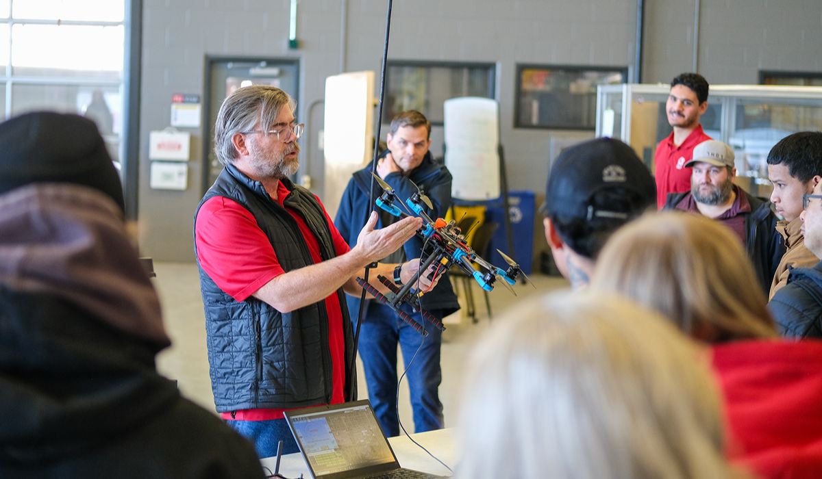 Person demonstrating a drone to a small group indoors.
