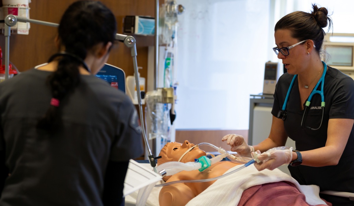 Two healthcare professionals in scrubs practice respiratory care techniques on a medical training mannequin connected to ventilation equipment in a clinical simulation lab.