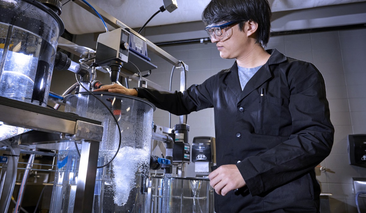 A researcher in a lab coat and goggles is operating a scientific apparatus filled with liquid in a laboratory setting.