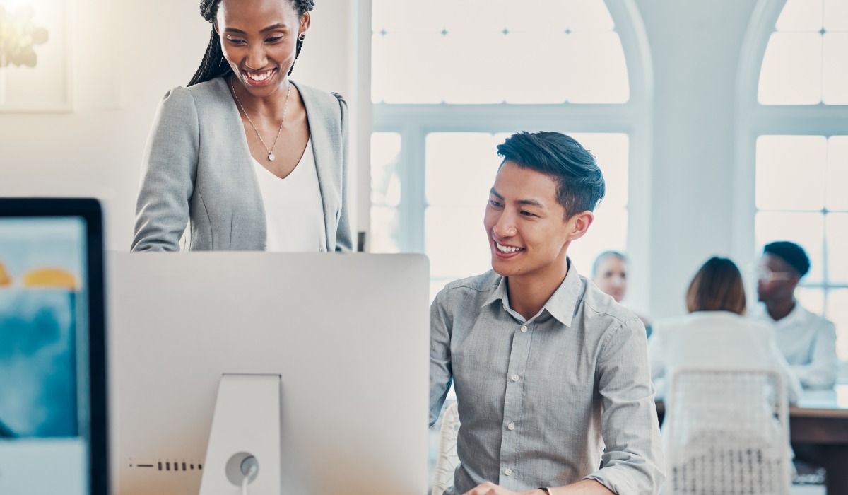 A professional interacting in a modern office environment, showcasing teamwork and collaboration between a woman in a blazer and a man at a computer.
