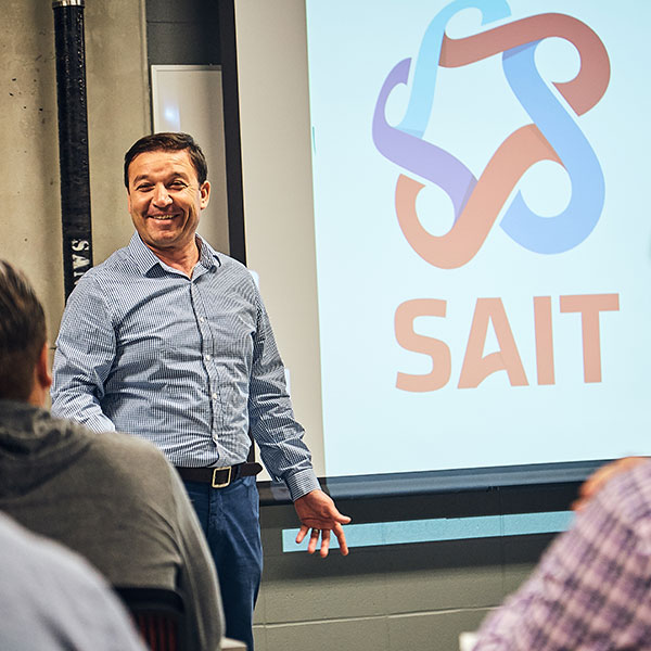 A SAIT instructor smiles while standing at the front of a classroom.