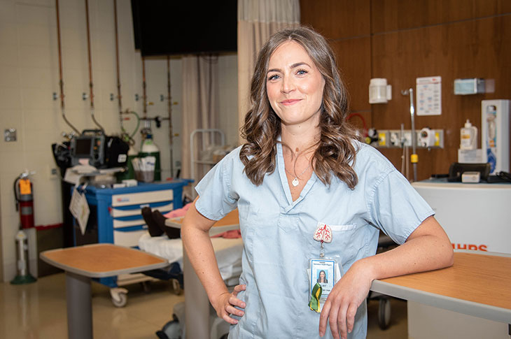 female Caucasian Respiratory therapist with long brown hair, posing in scrubs in work setting, 