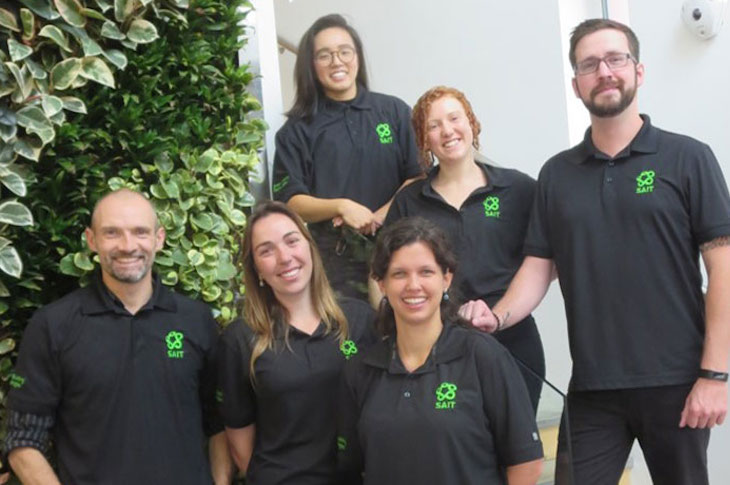 A group of people pose for a photo. They are wearing black shirts with a green logo