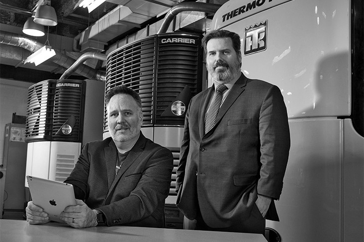 Two men stand are posed in front of industrial sizes coolers