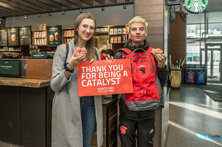 Two SAIT students hold up a sign that says "Thank you for being a catalyst."