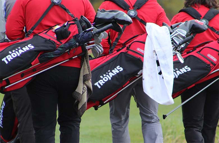 The SAIT Trojans golf team carrying golf bags.