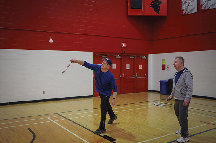 Two youquest members play badminton in the SAIT gymnasium.