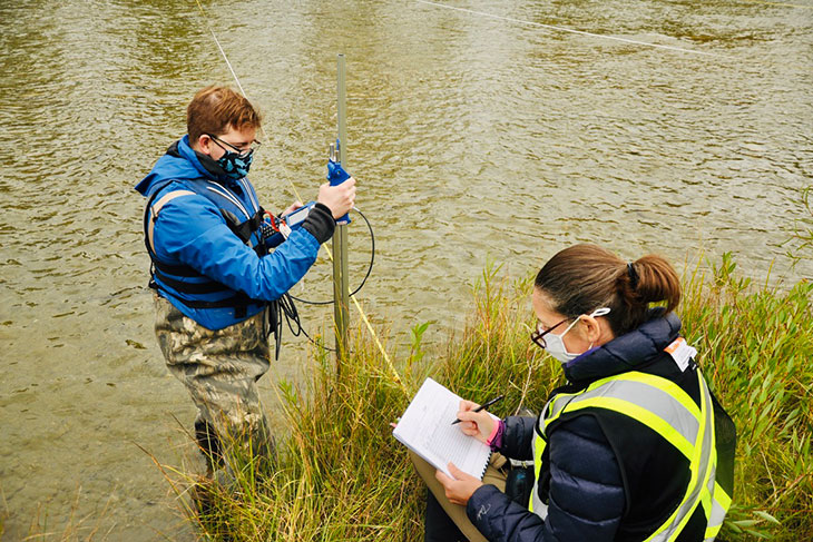 Students take water measurements while standing in a river