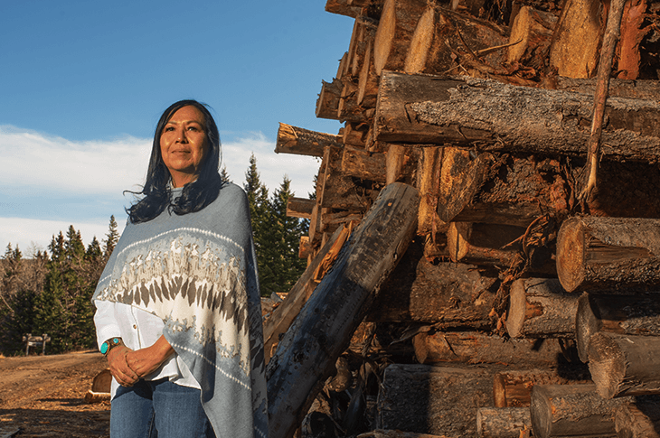 Indigenous woman standing in front of a wood pile at sawmill