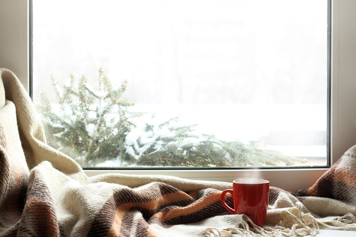 Mug with a hot drink placed in front of a window sill with a winter setting in the background