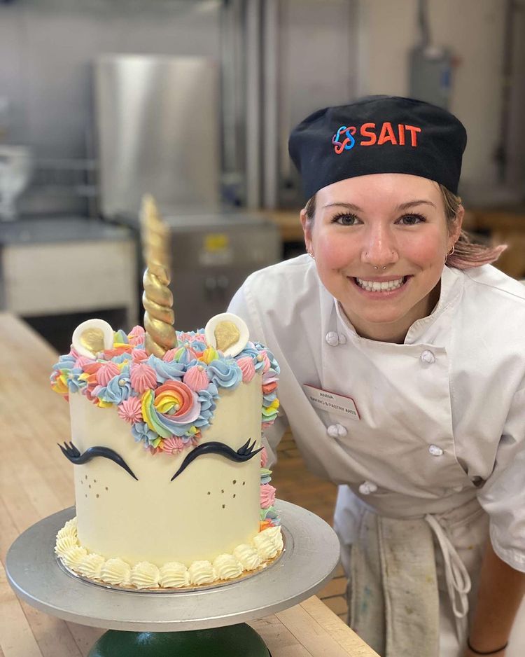 Student smiles at camera with a unicorn cake