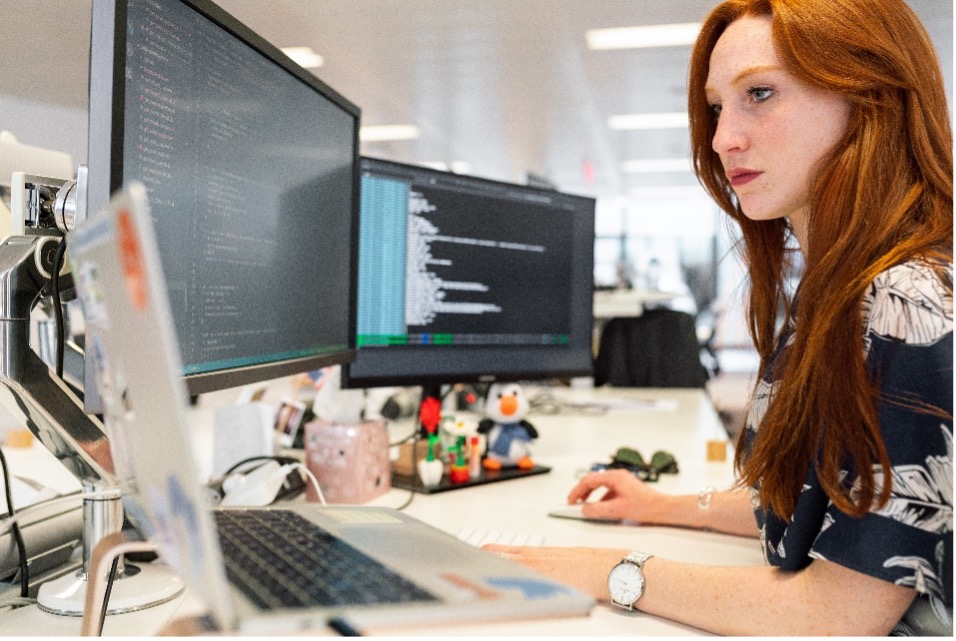 Business woman with red hair coding on a monitor