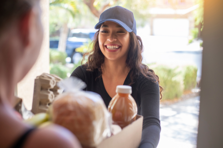 girl in a hat giving a box of food to a person