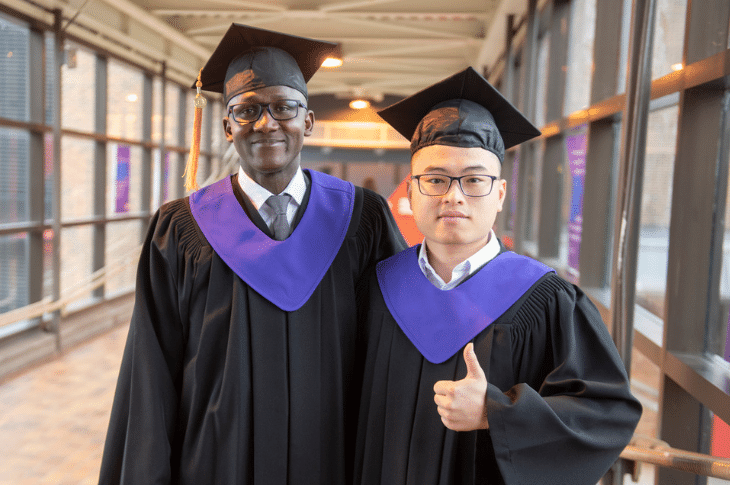 two SAIT graduates standing in a hallway smiling and giving a thumbs up