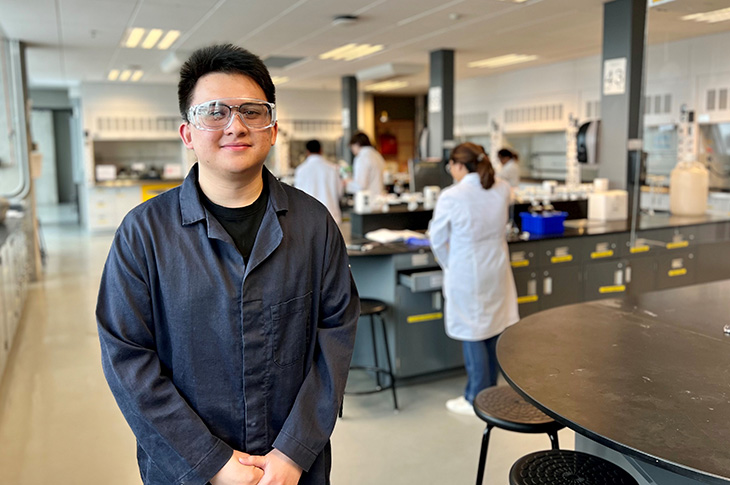 SAIT student King Veloso stands in a laboratory at SAIT smiling. Other students work in the background in the lab.