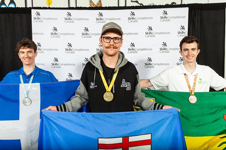 Thomas Jasonson smiles while holding the flag of Alberta and wearing a gold medal from the National Skills competition