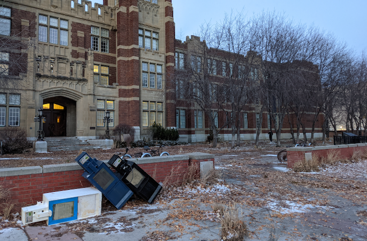 Rusted newspaper boxes sit tipped over in front of SAIT’s Heritage Hall.