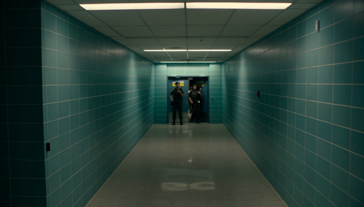 Two guards stand in front of a door at the end of a blue hallway in this shot featured in The Last of Us.