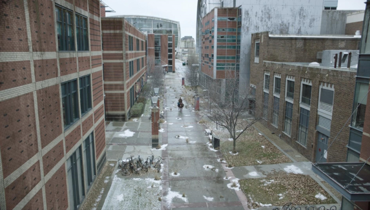 An overhead shot of Joel and Ellie as they ride a horse through SAIT’s campus. Trees and a red-bricked building are on either side of them.