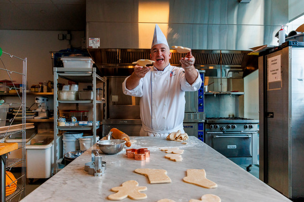 Chef Kevin Conniff stands in SAIT teaching kitchen throwing cookies towards the camera.