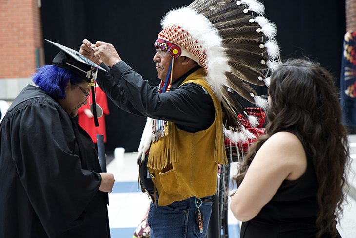 A medallion is placed on a graduate by an Elder in a traditional headdress