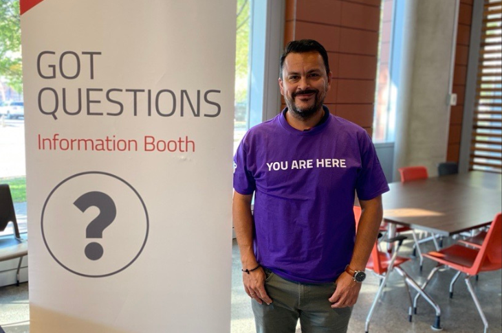 SAIT grad volunteer standing next to a Got Questions sign at new student orientation