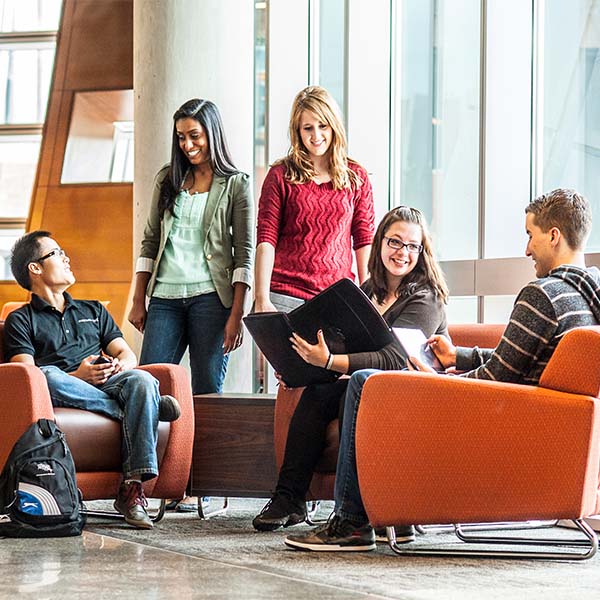 A group of students gather in a common area on campus and chat.