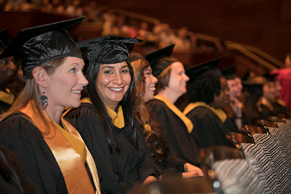 School of Business graduates wearing their cap and gowns sit in the Southern Alberta Jubilee Auditorium for their convocation ceremony.