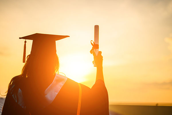 A graduate is holding her parchment up. She is silhouetted by the sun.