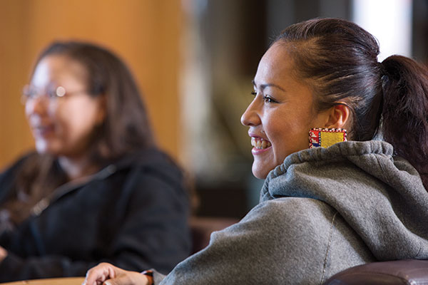 An Indigenous woman with colourful, beaded earrings smiles at someone off camera.