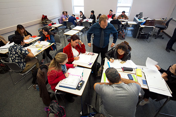 An instructor assists a group of students sitting in a classroom.