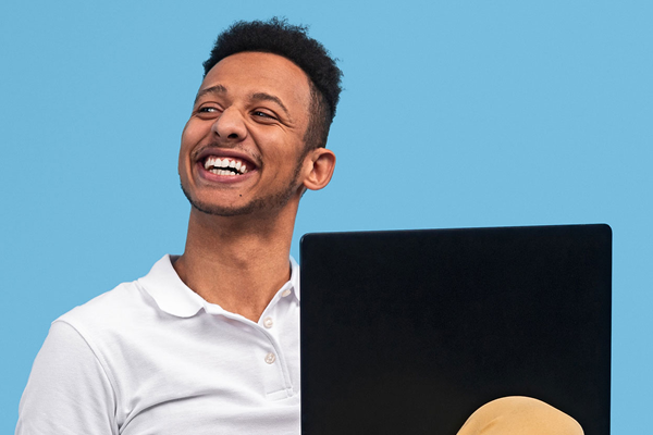 Man smiling with a laptop on his lap in a blue background