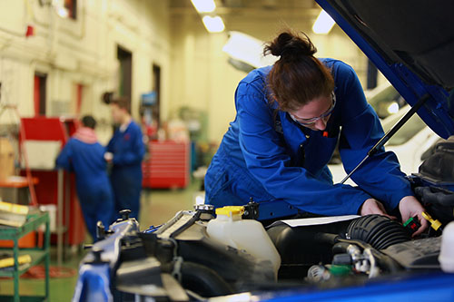 An Automotive Service Technology student works in the engine of a vehicle.