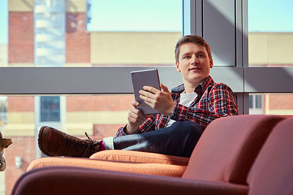 A student sits in Johnson-Cobbe building holding a tablet. 