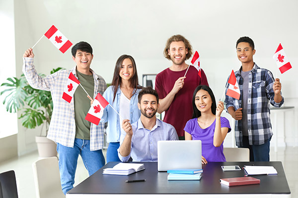 A group of students sits around a laptop holding small Canada flags.
