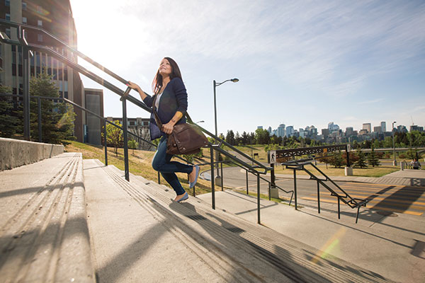 A young woman walks up a stairwell on SAIT campus. The Senator Burns Building is seen behind her.