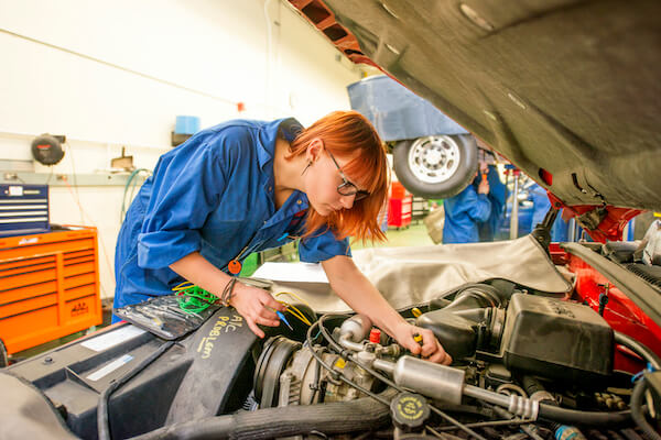 A person woith red hair looks under the hood of a car