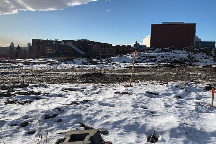 View of Campus Centre construction site from the SAIT Parkade entrance showing snow and ice on the flat dirt site with AUArts in the background.