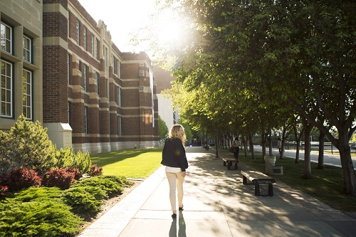 A woman walks along the sidewalk in front of Heritage Hall. She looks back at the camera.