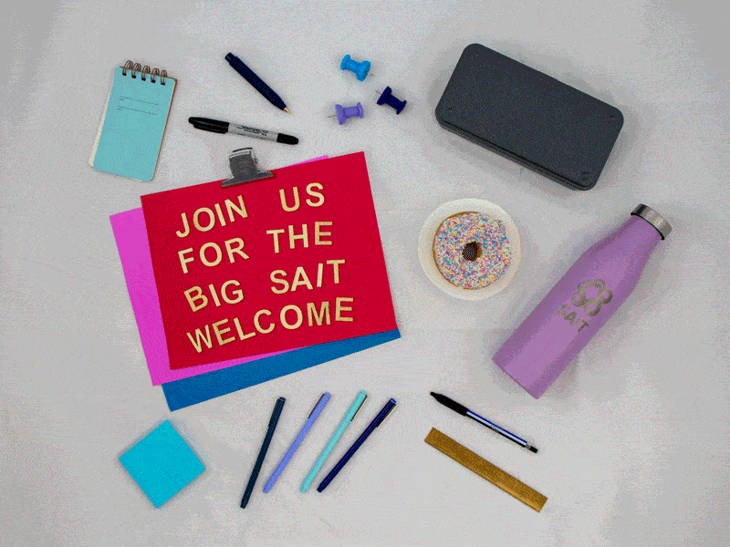 An assortment of school supplies scattered on a table, including a notebook, pens, water bottle and pins. The front of the notebook reads "Join us for the big SAIT welcome."