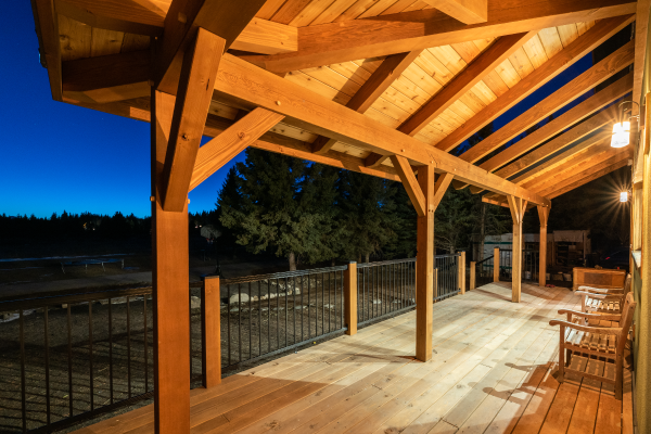 The covered veranda creates an inviting and protective gathering space, constructed with locally-sourced lumber and custom-milled timbers.