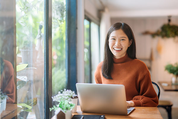Woman in orange sweater smiling with laptop