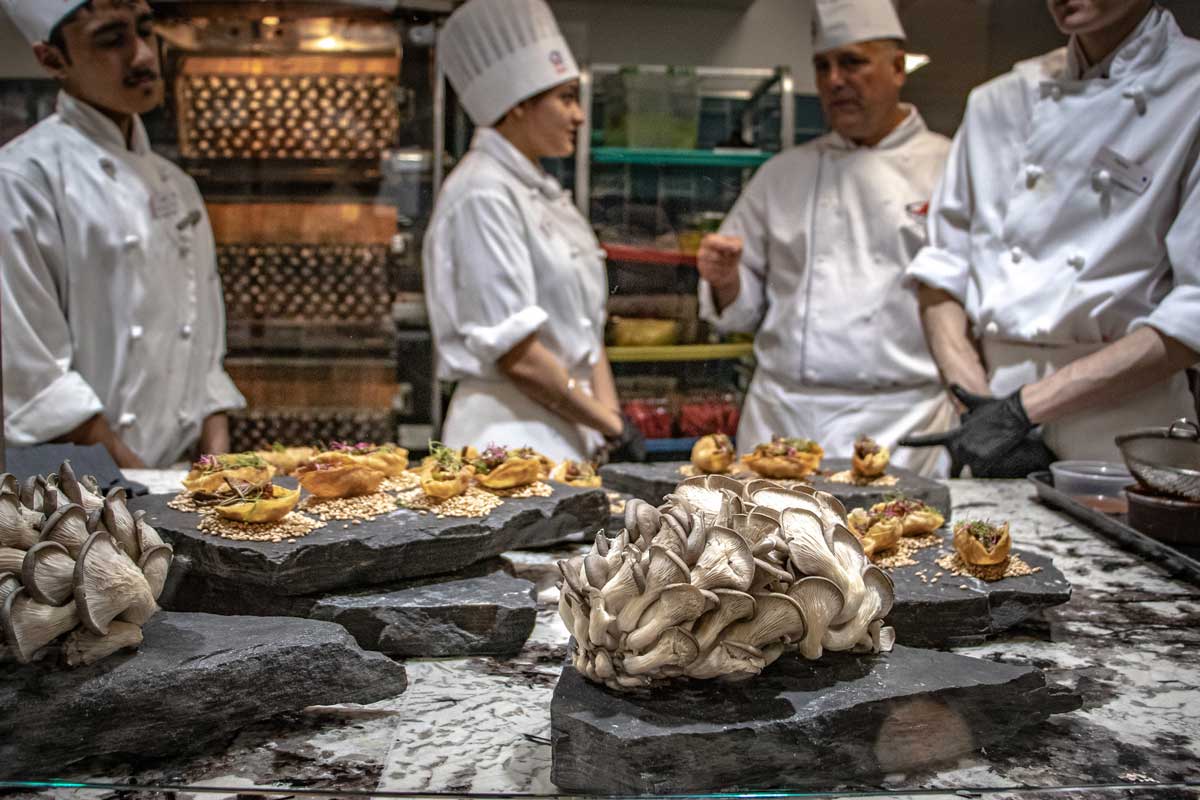 Students and their instructor in the Culinary Campus International Market kitchen discuss the oyster mushrooms displayed in the foreground