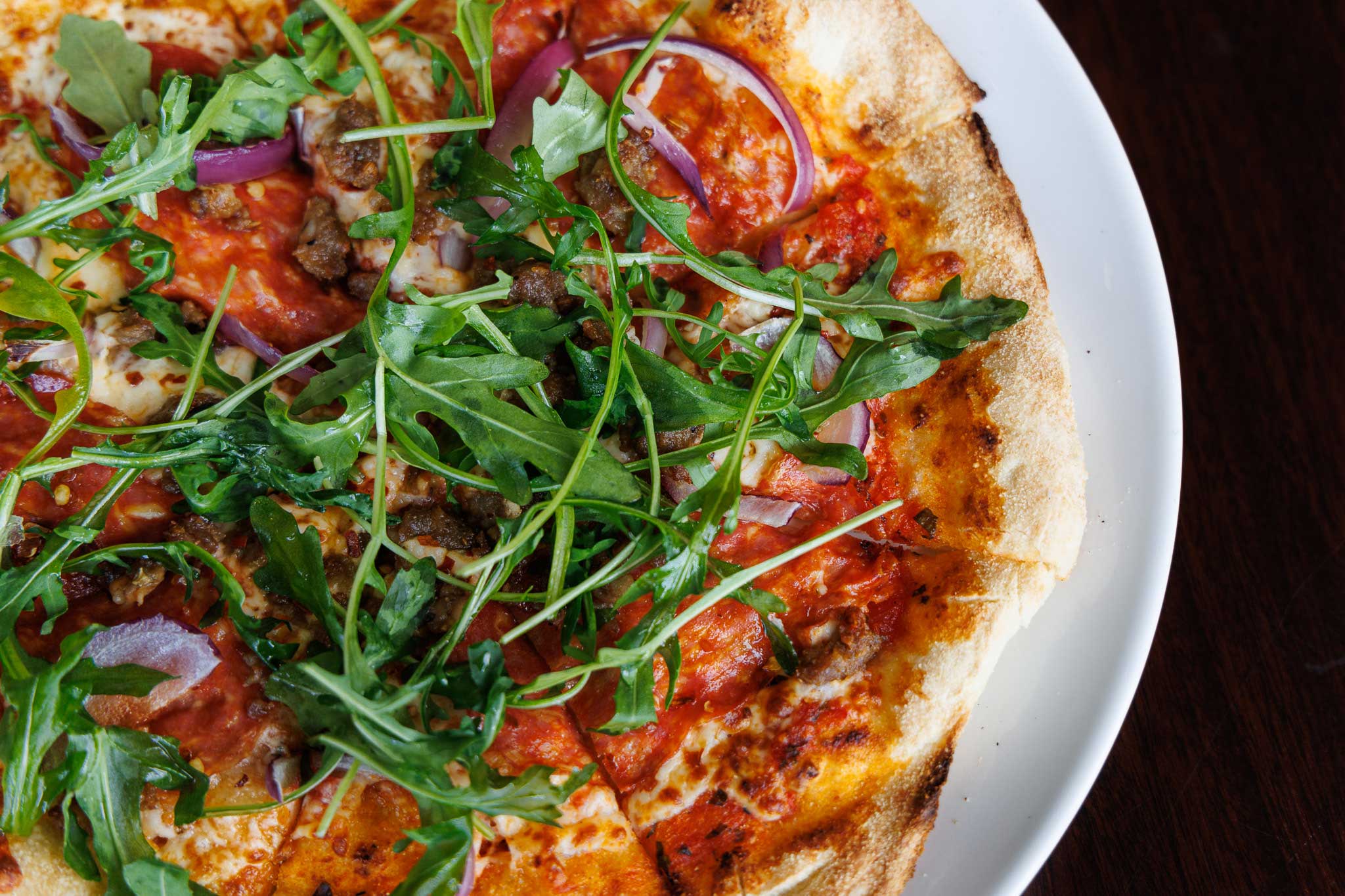 a close up of calabrese pizza topped with red onions and arugula