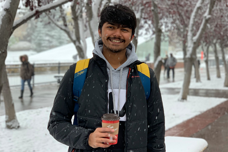 Student holding coffee in snow smiling